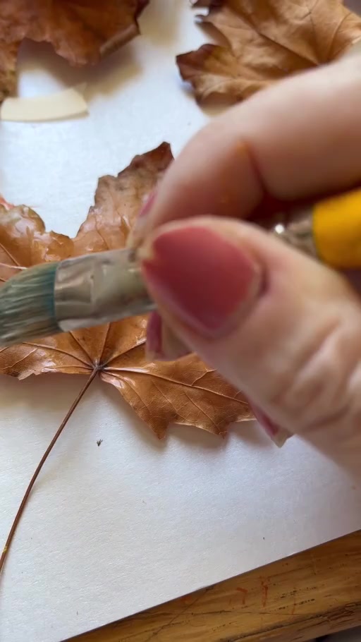 A hand brushing a warm metallic colour across a dry leaf